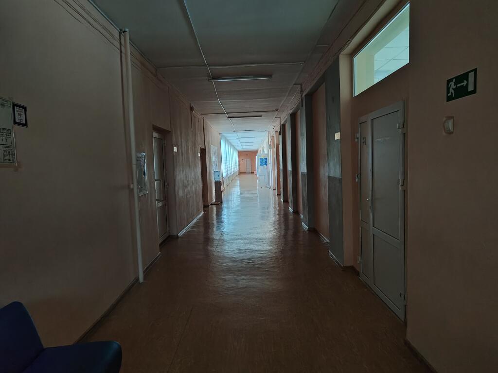 Длинный пустой коридор с оранжевыми стенами, дверями, окнами со шторами и скамейками вдоль стен (2 из 5)