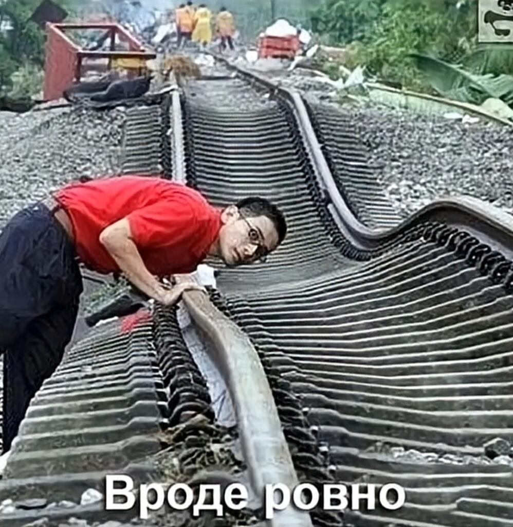 Мужчина в красной футболке наклонился над сильно искривленными железнодорожными путями, пытаясь оценить их ровность