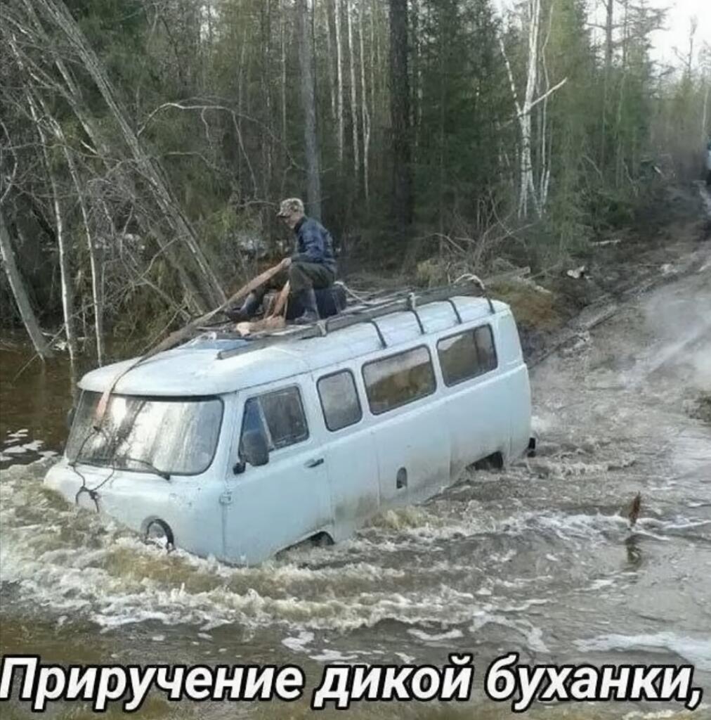 Белый фургон УАЗ Буханка стоит в бурной реке, а человек сидит на крыше и держится за багажник, как наездник на лошади