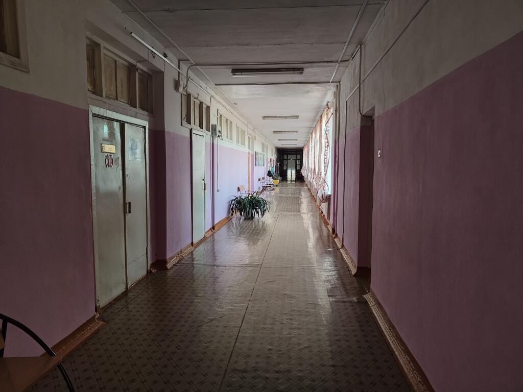 Длинный пустой коридор с оранжевыми стенами, дверями, окнами со шторами и скамейками вдоль стен (5 из 5)
