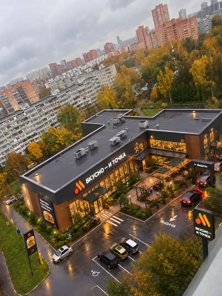 Желтое здание школы и припаркованные машины видны сверху вниз, вокруг растут деревья с осенней листвой (2 из 2)
