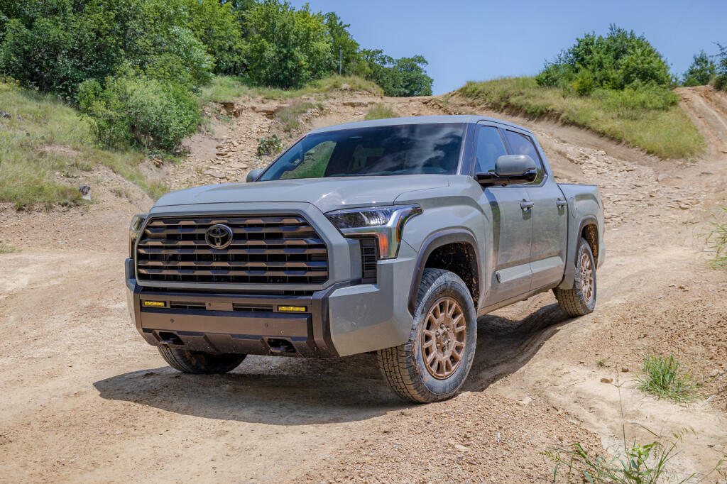 Серый пикап Toyota Tundra едет по грунтовой дороге среди кустов и травы под голубым небом