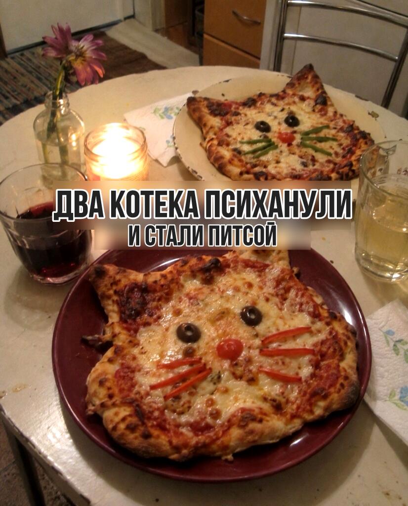 Две пиццы, испеченные в виде кошачьих мордочек с оливками и овощами, стоят на столе со свечами и напитками. Надпись: Два котика психанули и стали пиццей.
