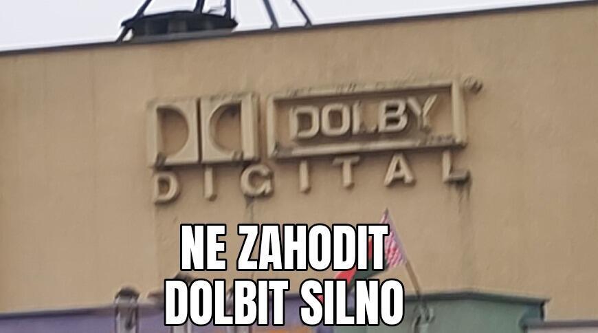 Надпись Dolby Digital на стене здания, под ней мемный текст на латинице, рядом виден флаг